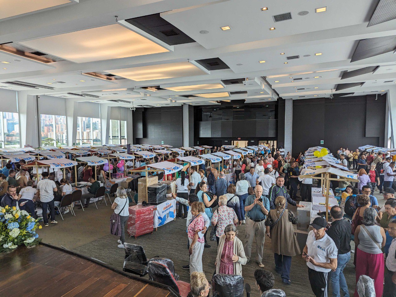 La reventa transfronteriza de importación EC es un evento interior a gran escala en el que un gran número de personas se paran y conversan alrededor de una mesa con varios artículos en exhibición en una sala con grandes ventanales y vistas a la ciudad.